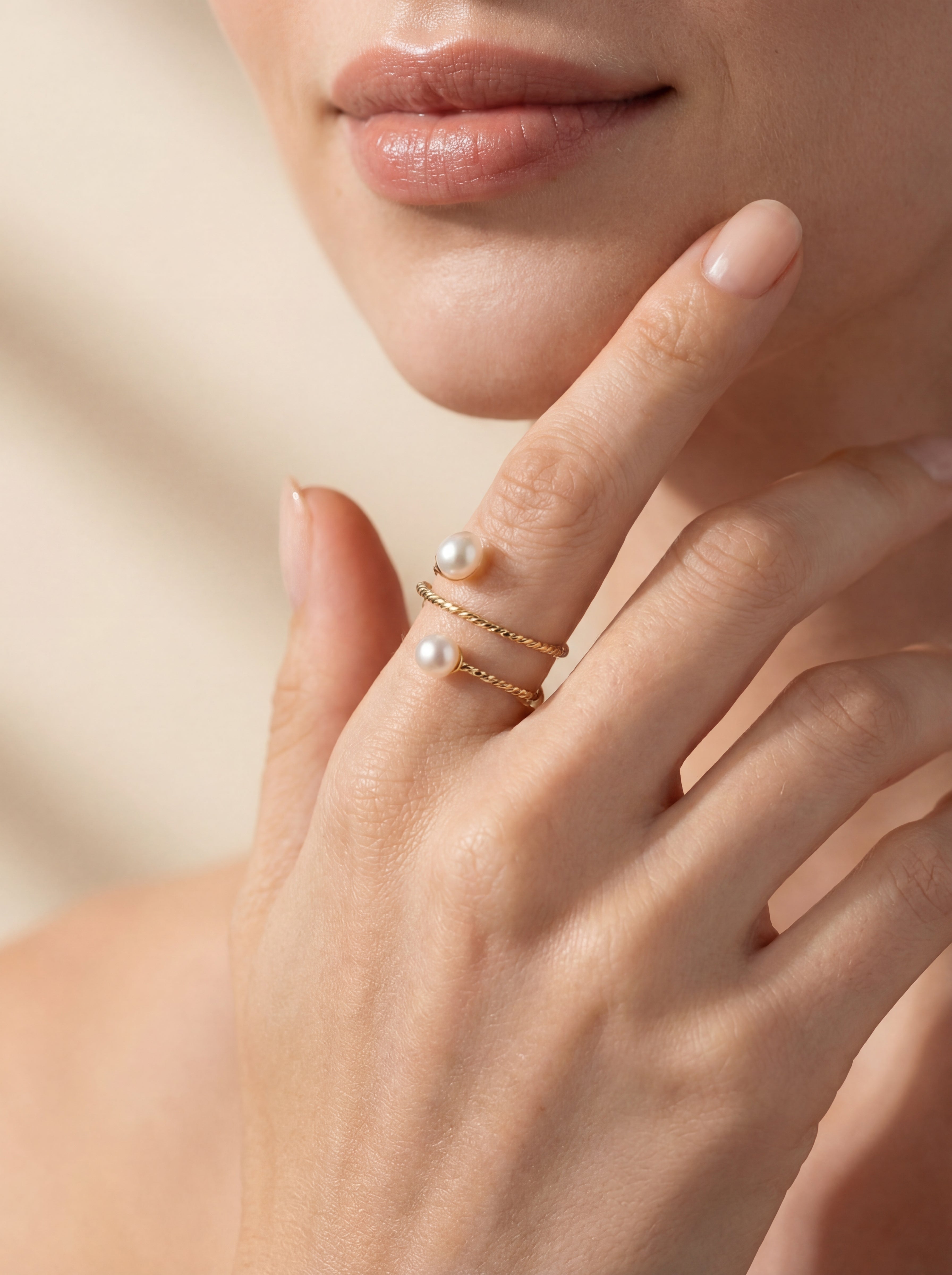 Close-up of a hand wearing a gold ring with pearls on a neutral background
