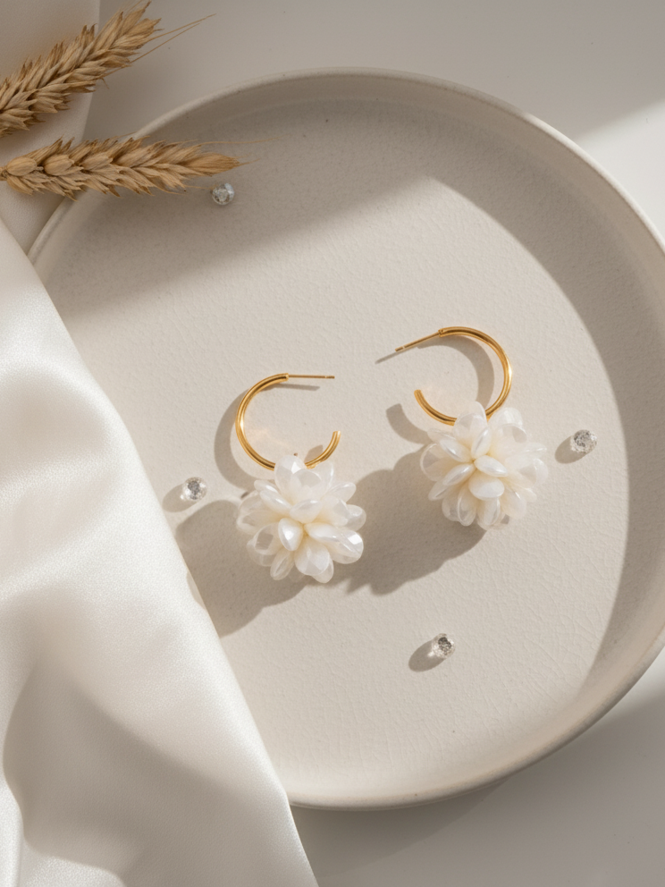 Gold hoop earrings with white floral designs on a beige plate with wheat stalks.