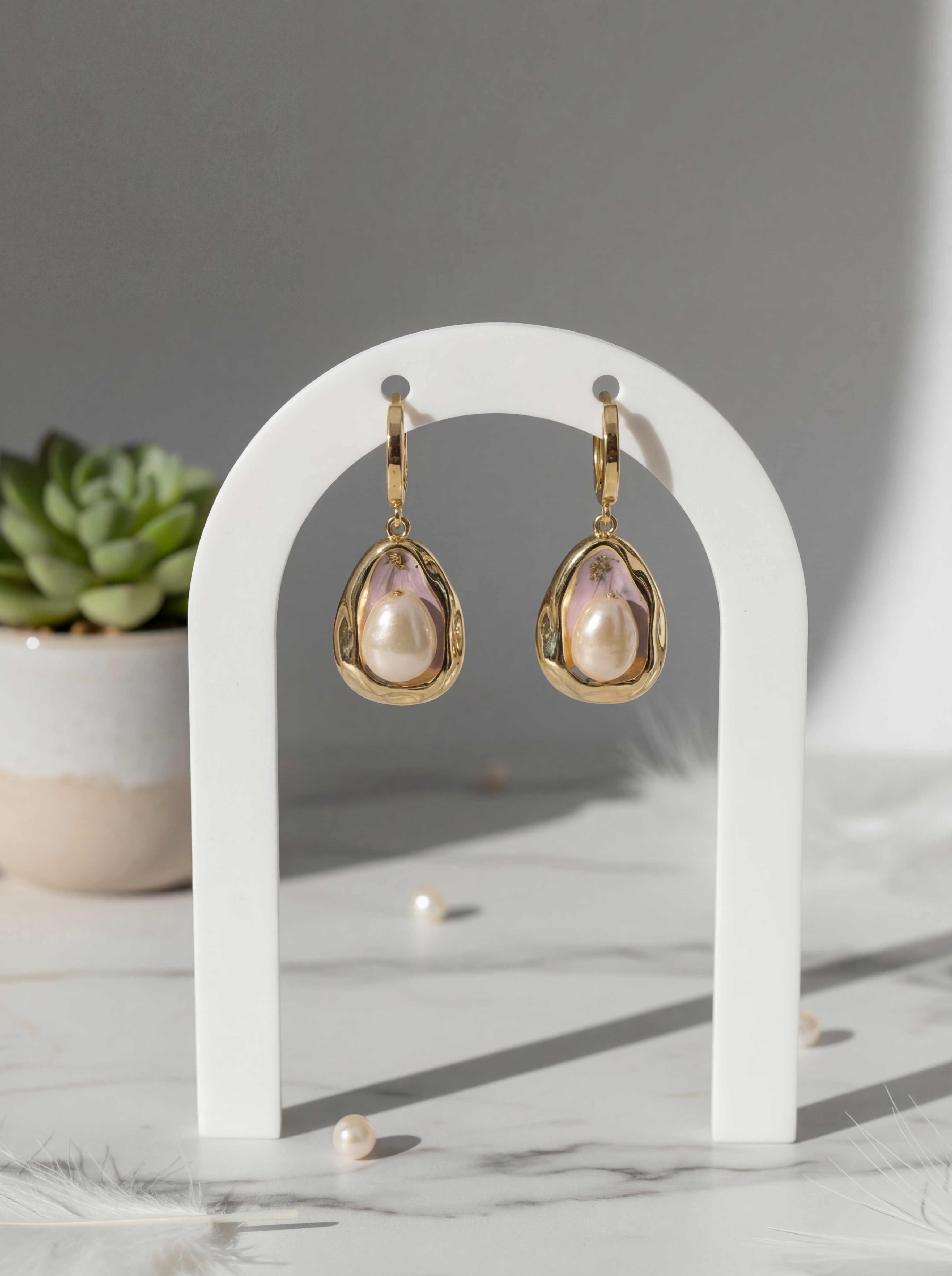 Gold earrings with pink gemstones on a white stand with a gray background