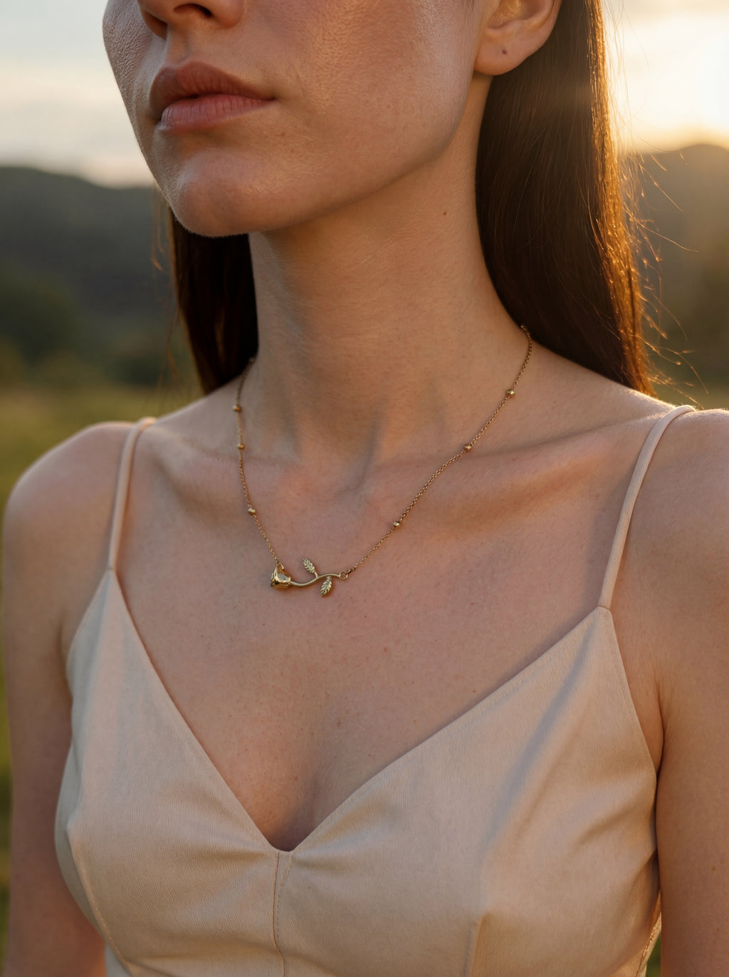 Woman wearing a delicate gold necklace with a blurred natural background