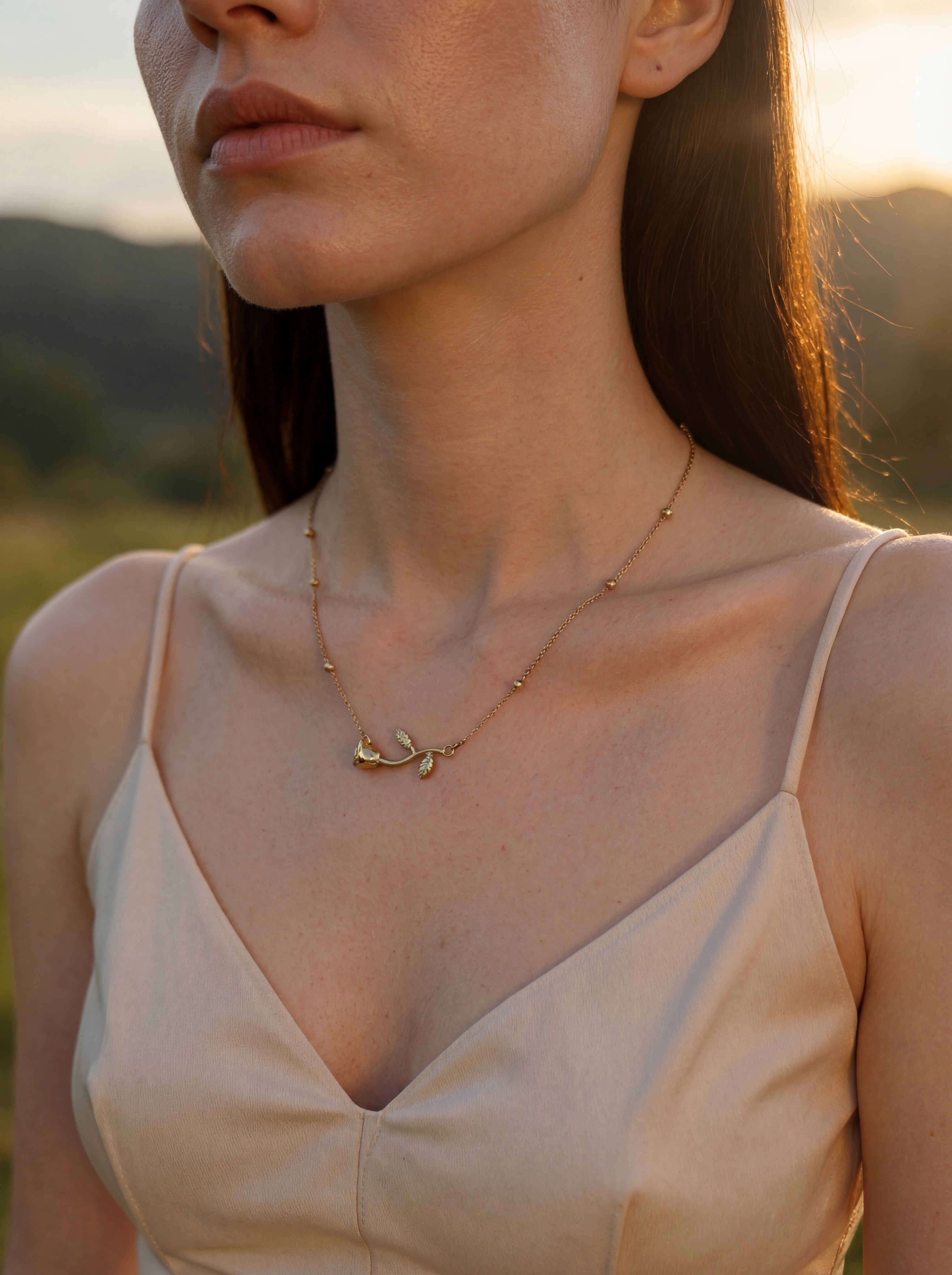 Woman wearing a delicate gold necklace with a blurred natural background