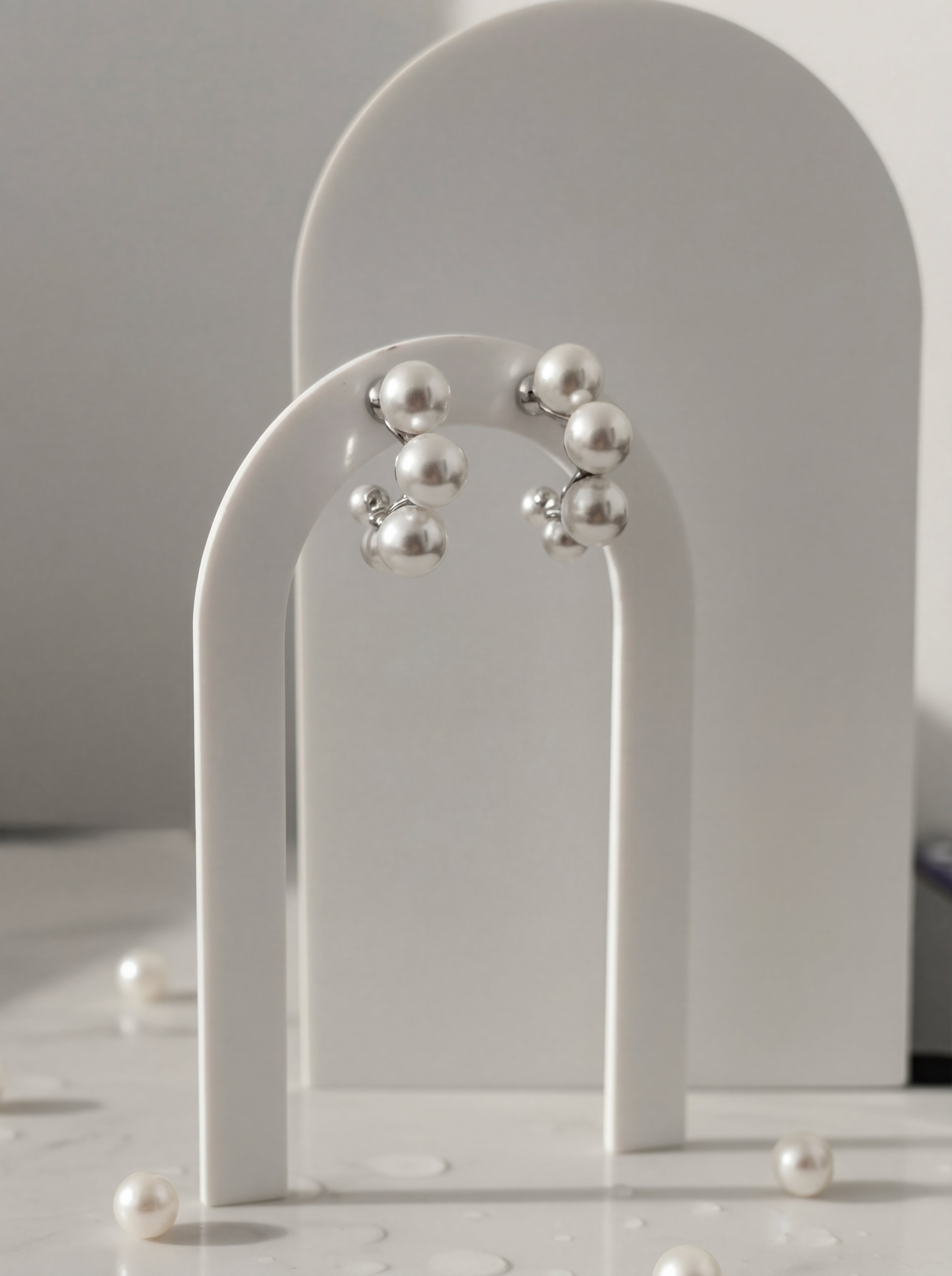 Pearl earrings on a white arch stand with a neutral background