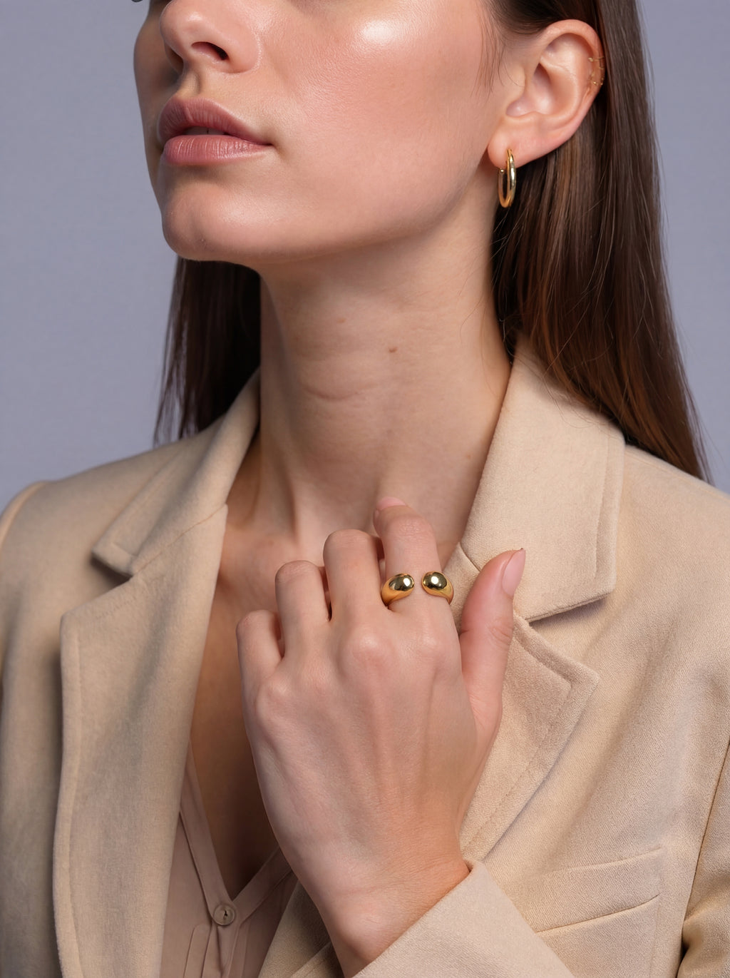 Woman wearing gold earrings and ring, with a neutral background