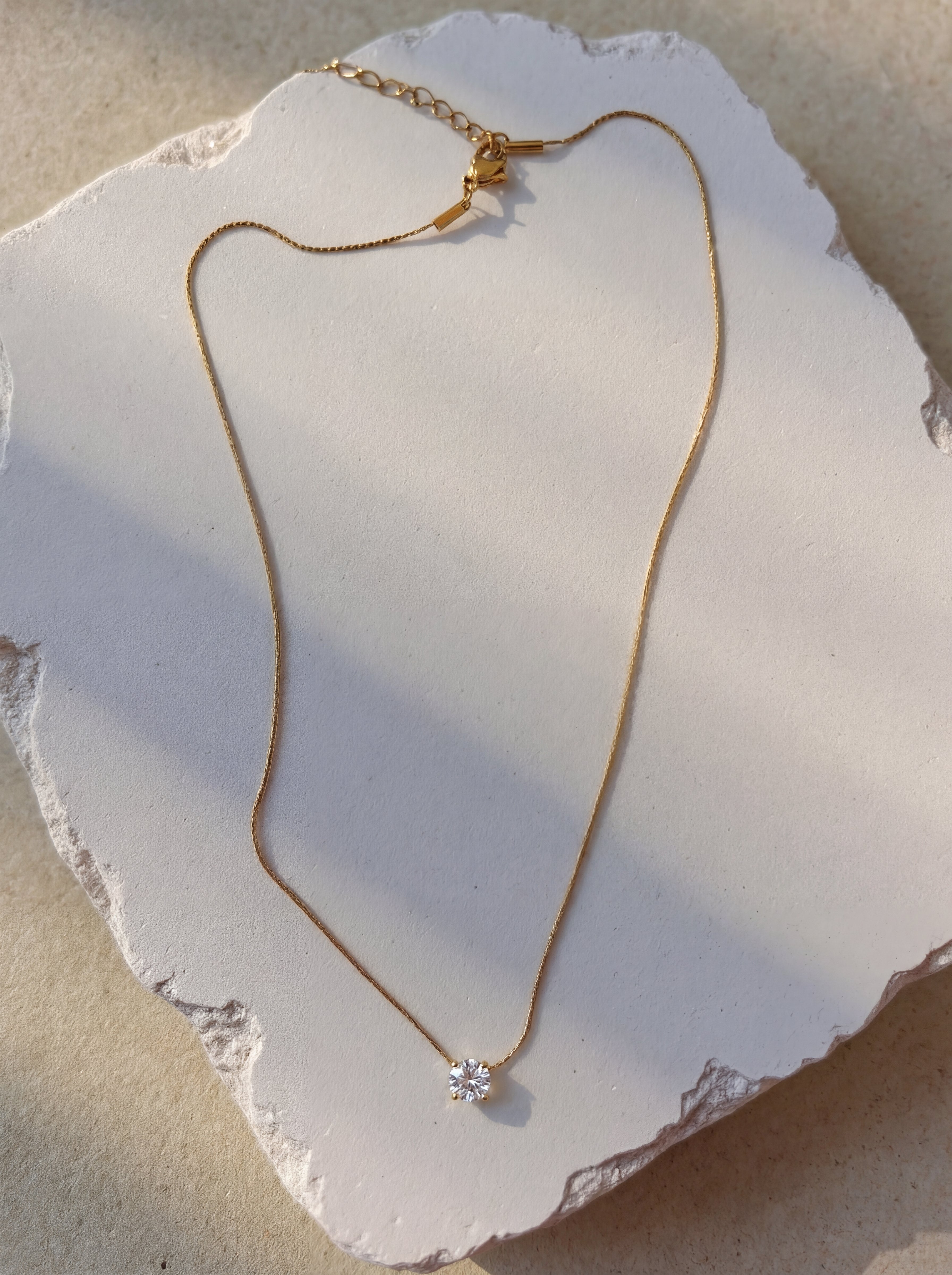 Gold necklace with a diamond pendant on a white stone surface