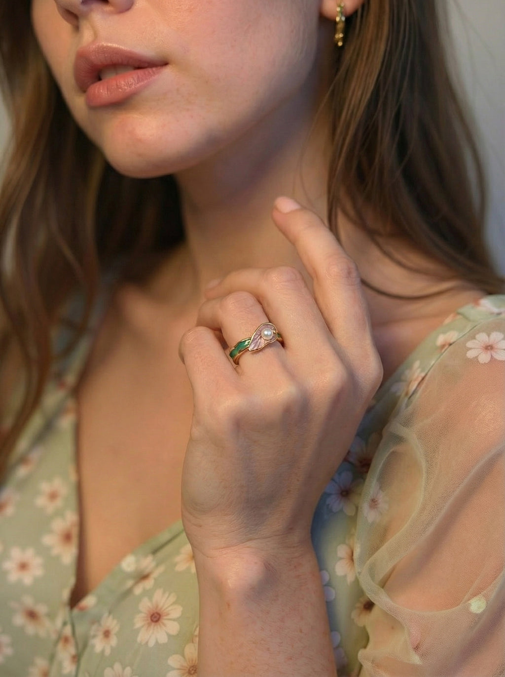 Close-up of a woman wearing a floral dress and a ring with a green gemstone.