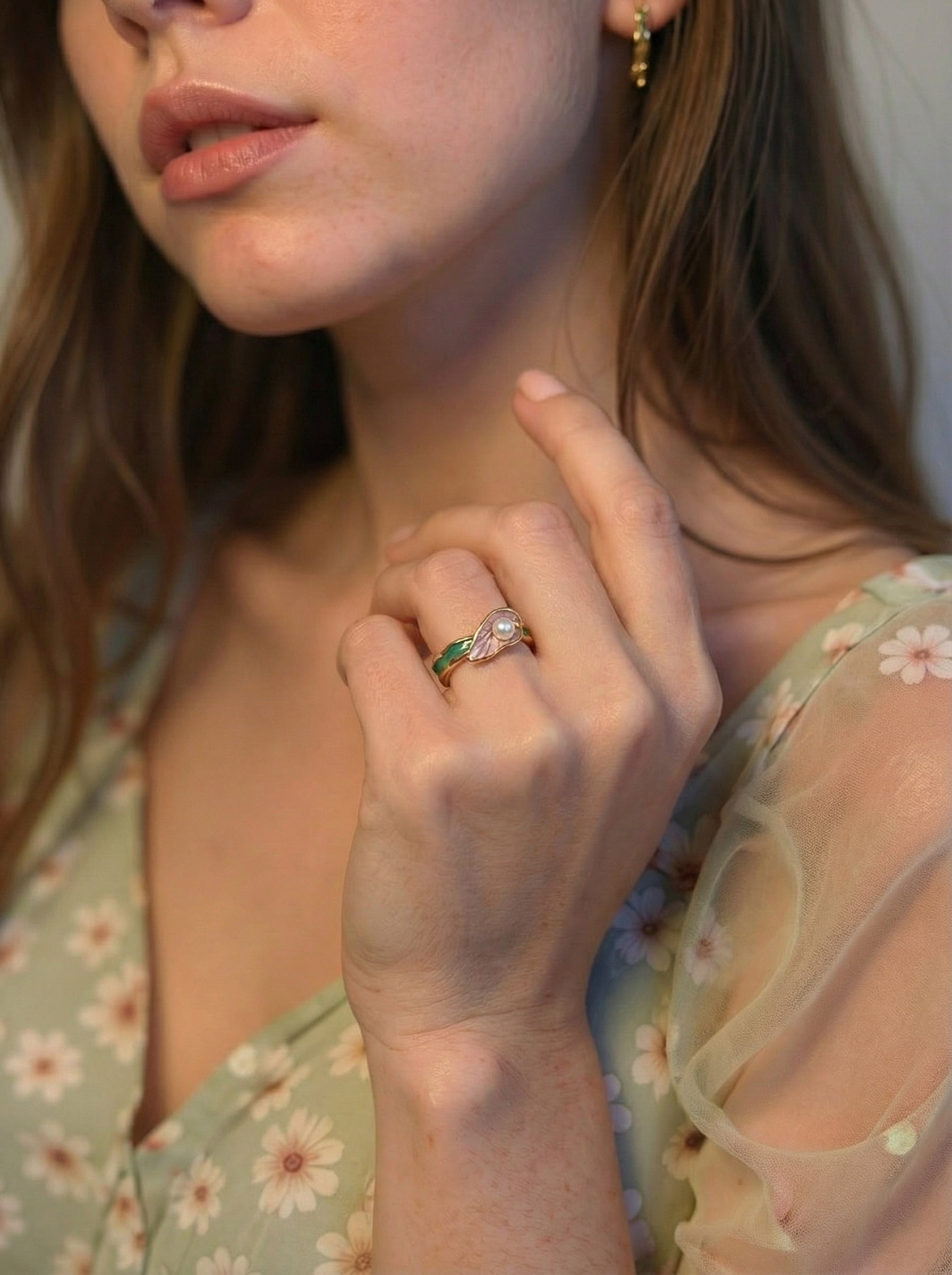 Close-up of a woman wearing a floral dress and a ring with a green gemstone.