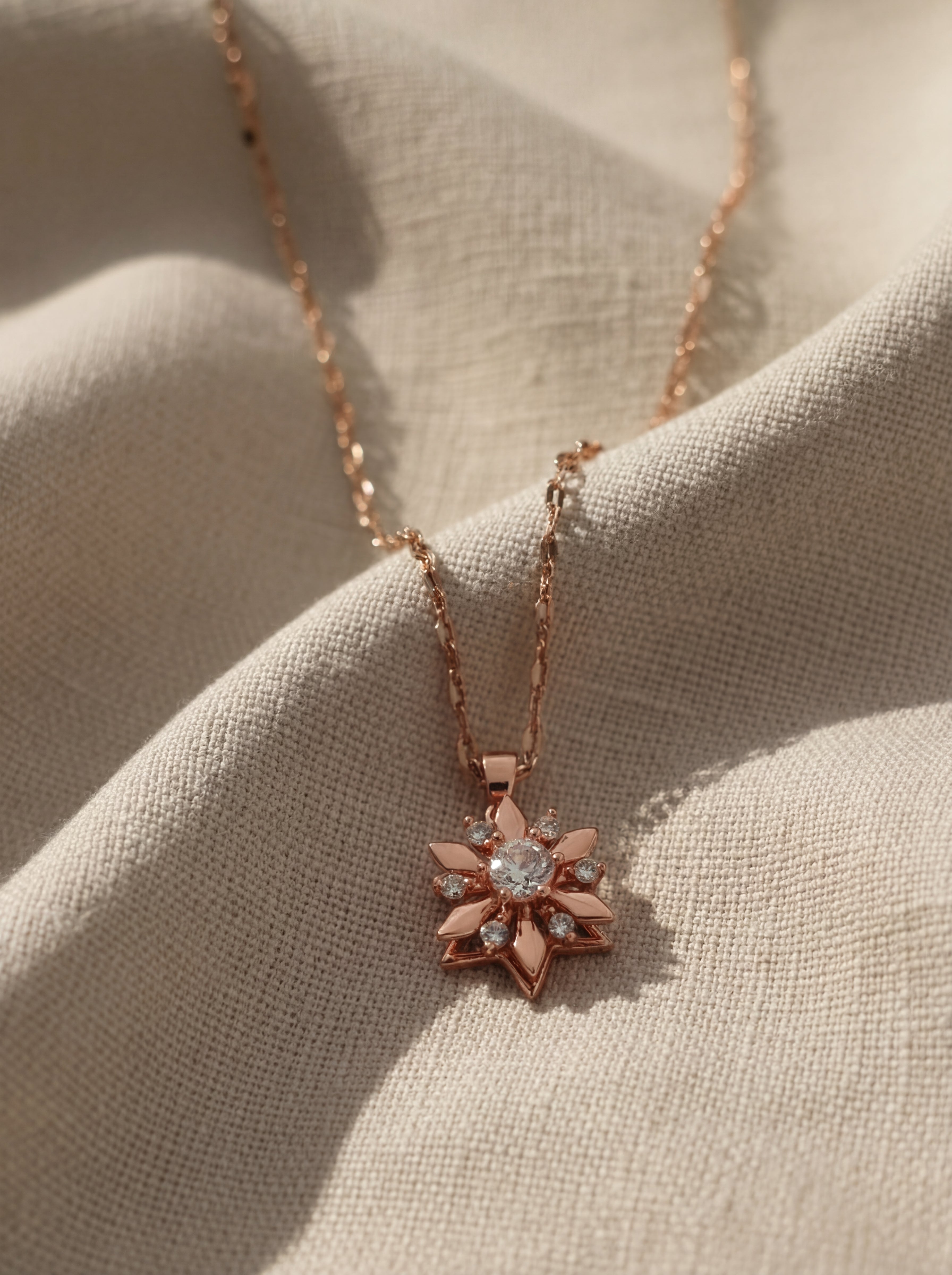 Rose gold necklace with a star-shaped pendant on beige fabric