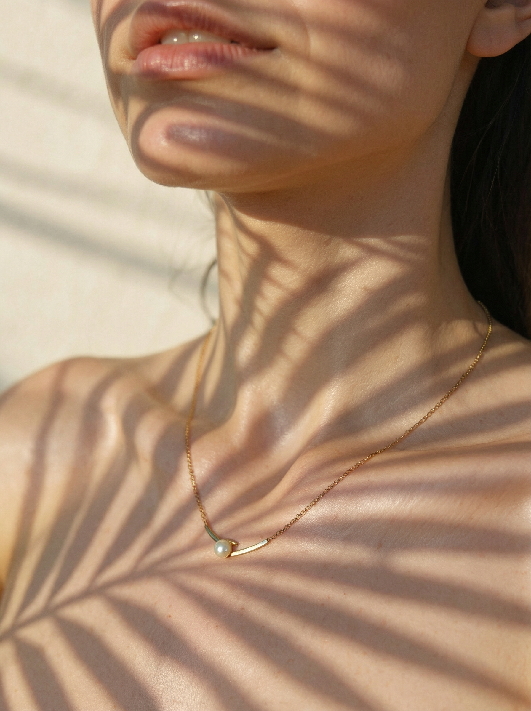 Necklace with a small pendant worn by a person, with palm leaf shadows on the skin.