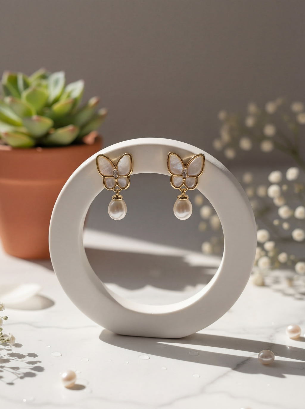 Butterfly-shaped earrings on a white circular stand with a plant in the background