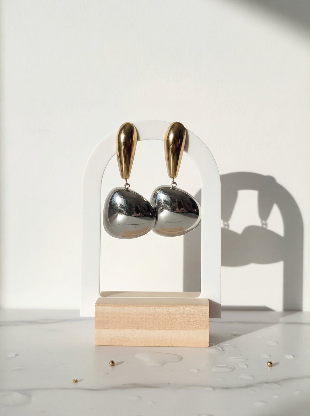 Gold and silver earrings on a clear stand with a wooden base against a white background