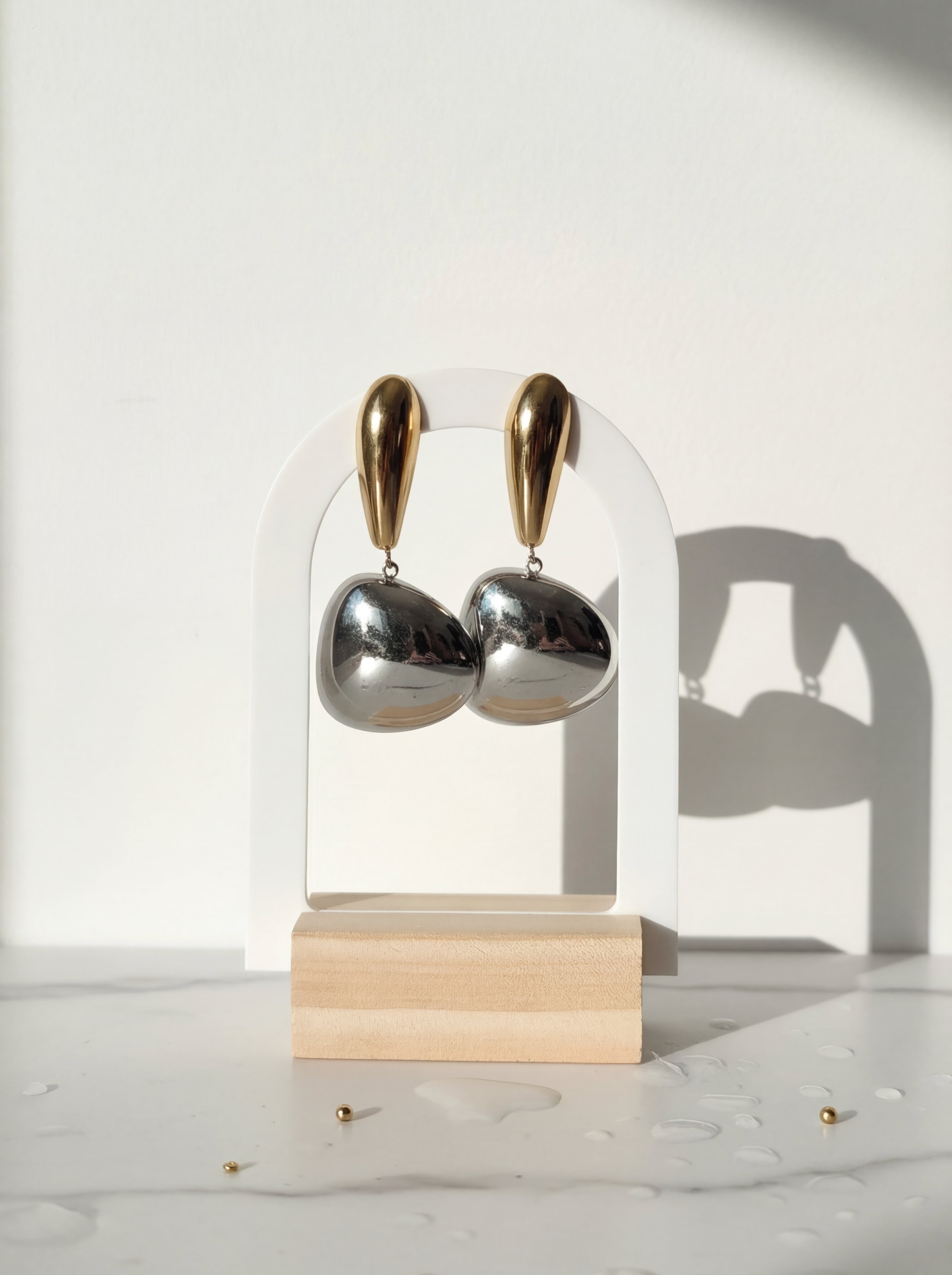 Gold and silver earrings on a clear stand with a wooden base against a white background