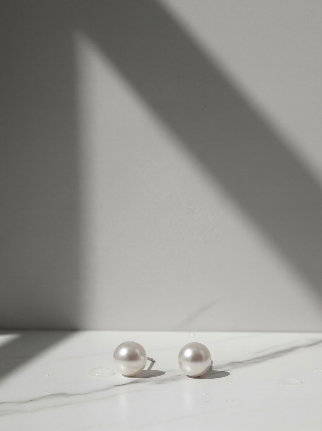 Pearl earrings on a white surface with a soft shadow on a light gray background