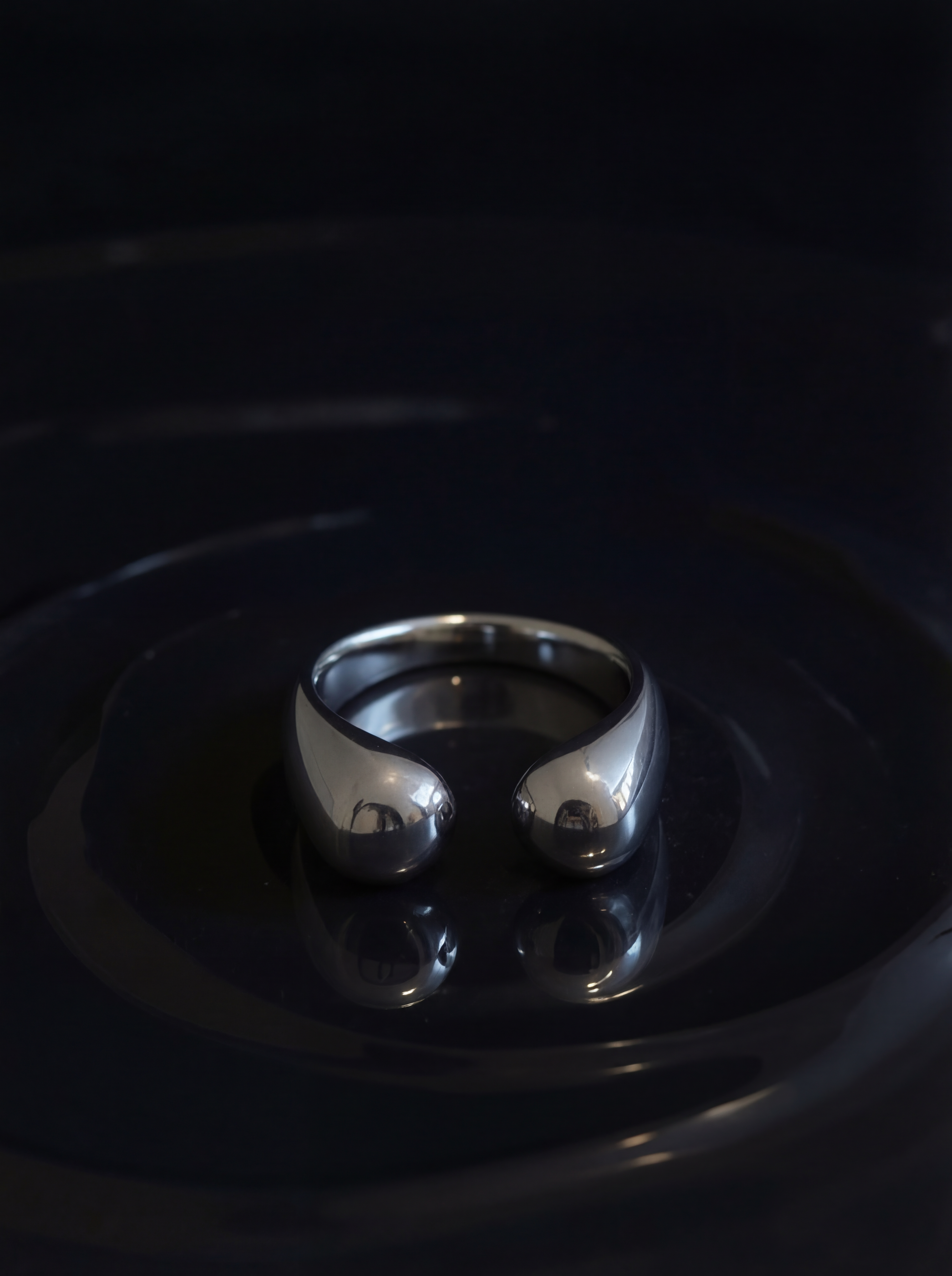 Silver ring on a reflective black surface with a dark background