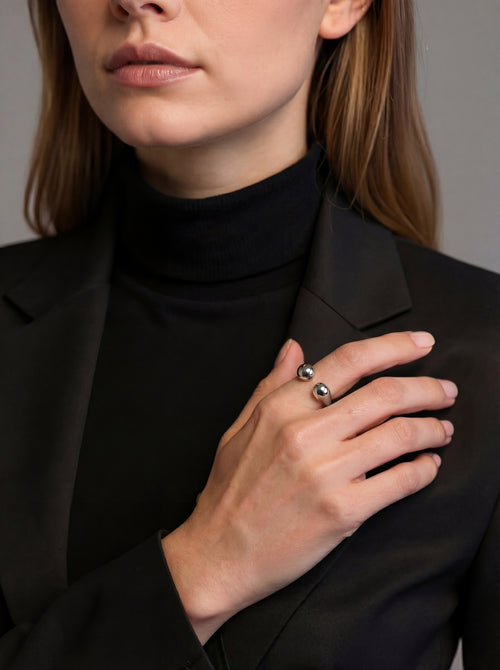 Person wearing a black turtleneck and black blazer with a close-up of their hand holding a small object.