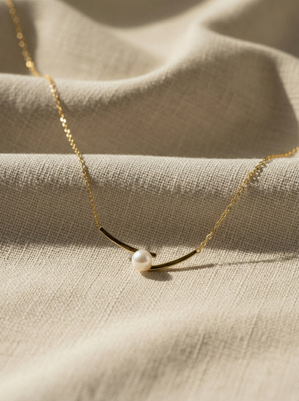 Delicate gold necklace with a pearl pendant on a beige fabric background