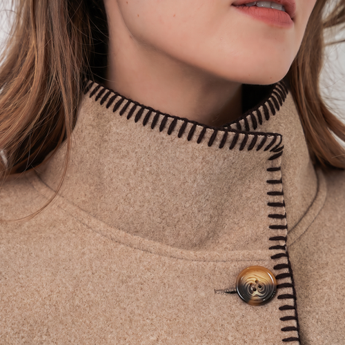 Close-up of a beige oversized poncho featuring brown blanket stitch detailing on collar.