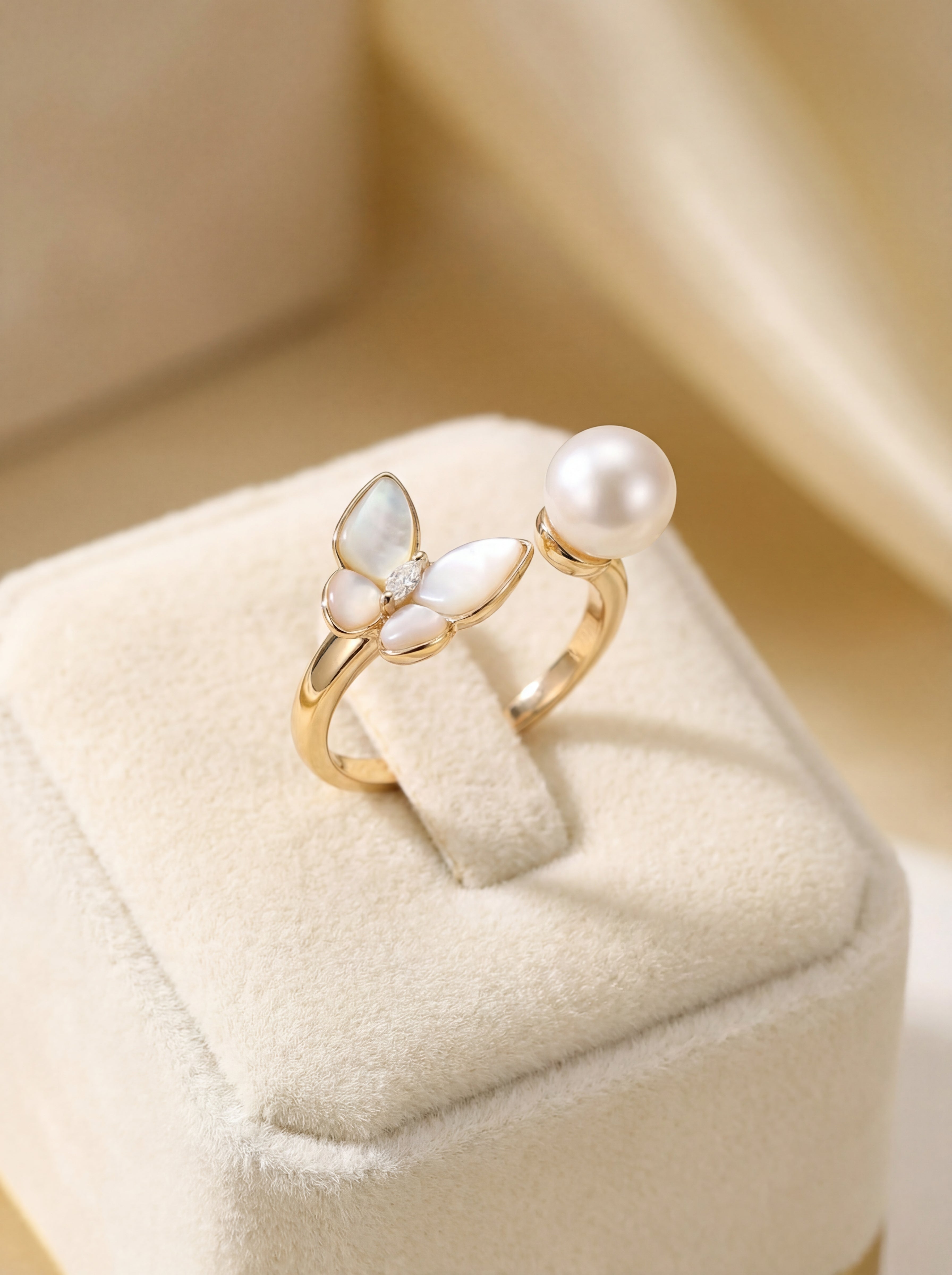 Gold ring with butterfly design and pearl on a beige cushion