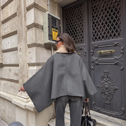 Woman wearing a grey oversized cape poncho with a beige faux-fur collar.