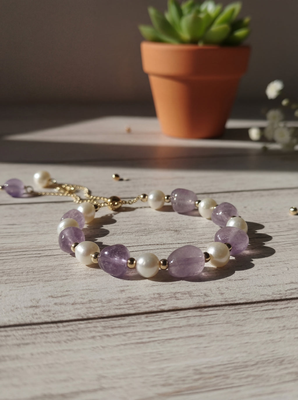 Amethyst and pearl bracelet on a wooden surface with a potted plant in the background