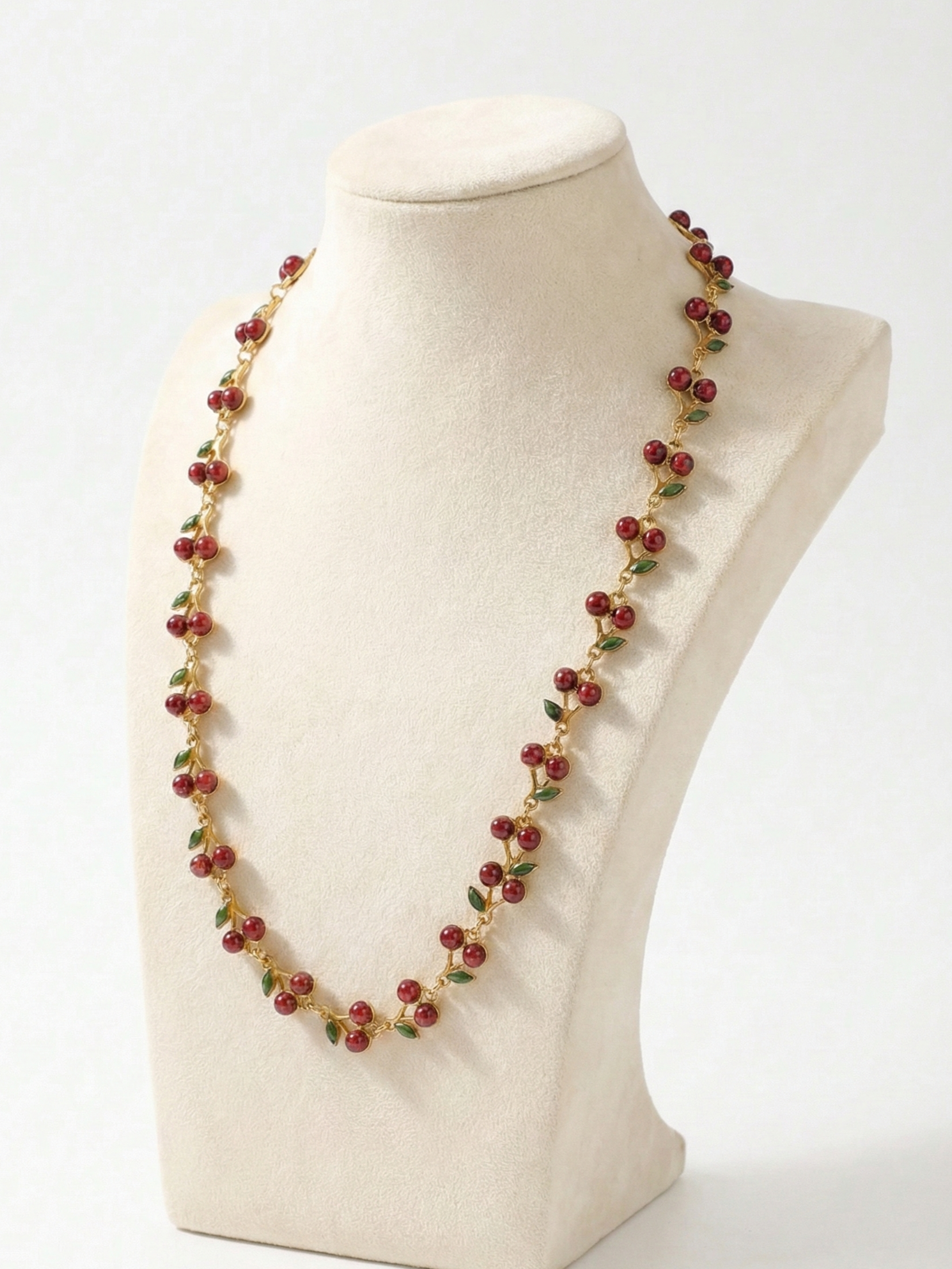 Necklace with red and green beads on a mannequin bust against a white background