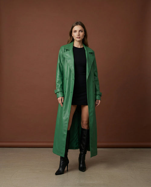 A model wearing an emerald green faux leather long trench coat over a black dress.