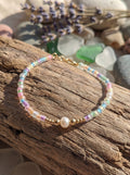 Multicolored beaded bracelet with a pearl on a wooden surface with pebbles in the background