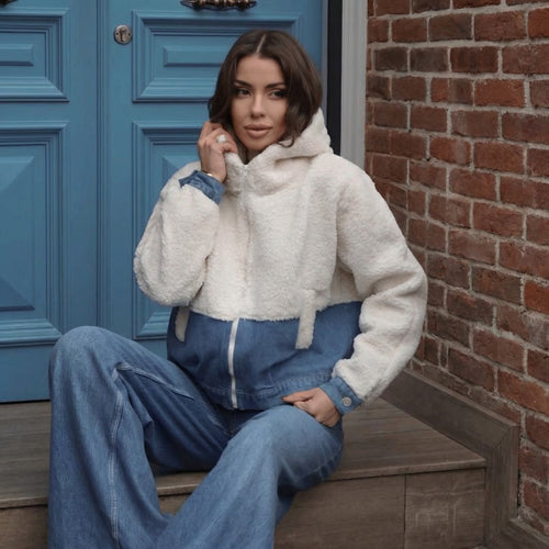 Una mujer que lleva una chaqueta bomber híbrida con capucha de suave forro polar blanco y mezclilla azul.