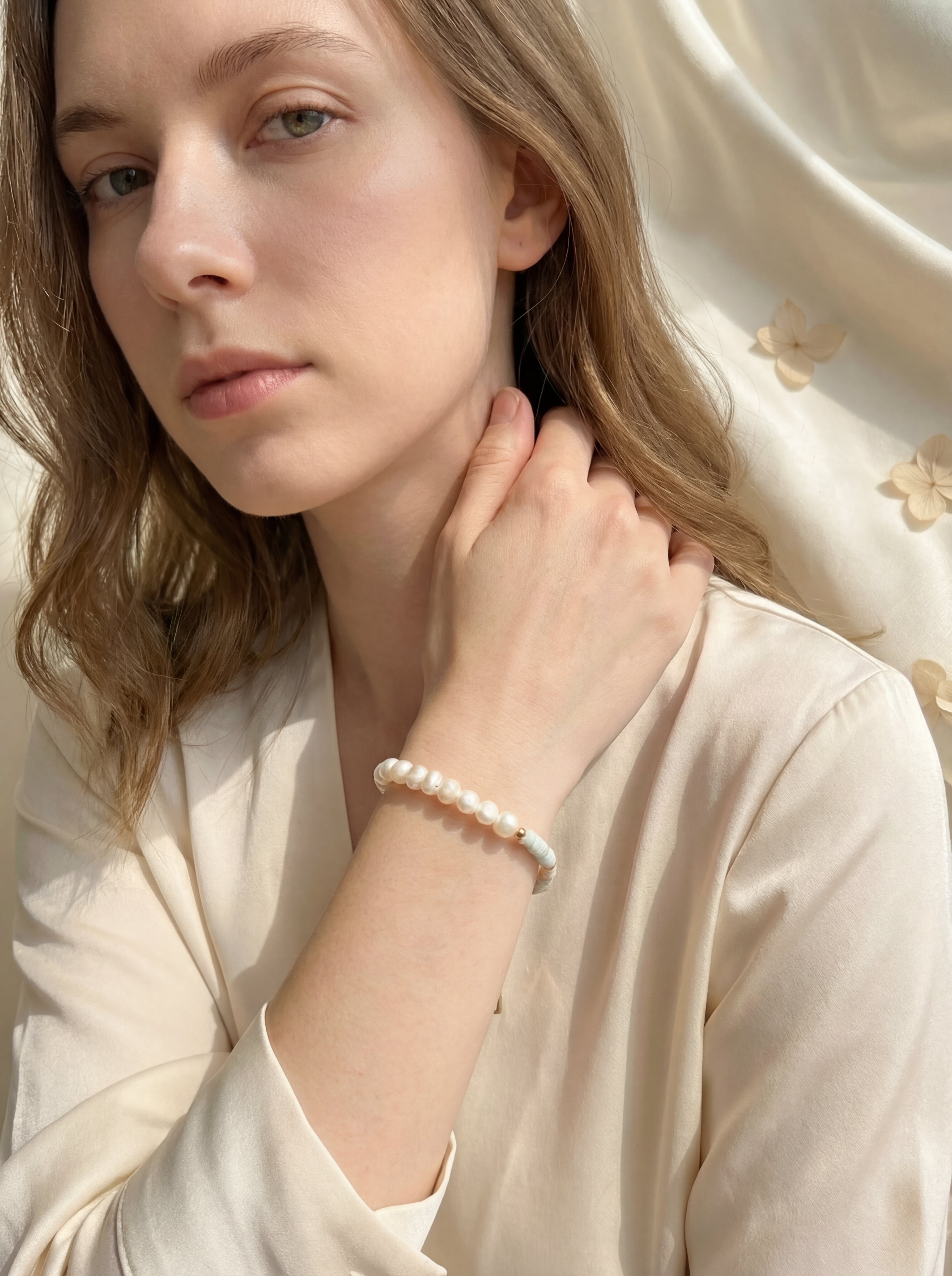 Woman wearing a pearl bracelet against a soft, neutral background