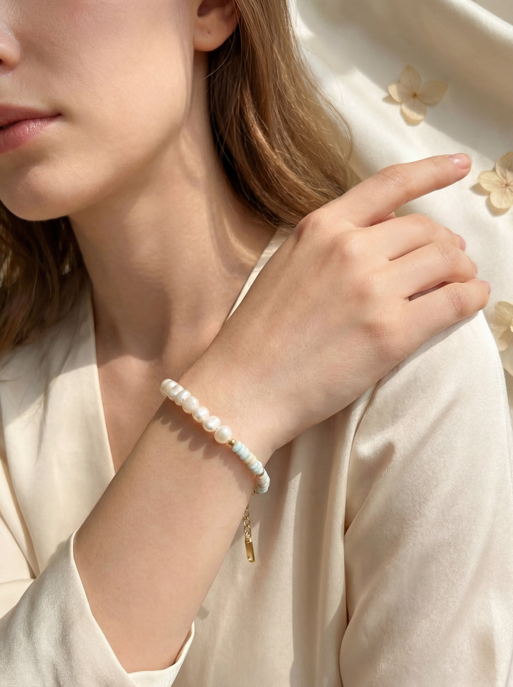 Close-up of a person wearing a pearl bracelet on a light background